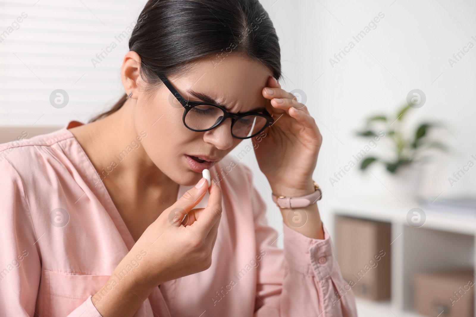 Photo of Young woman with pill suffering from headache at table indoors, space for text