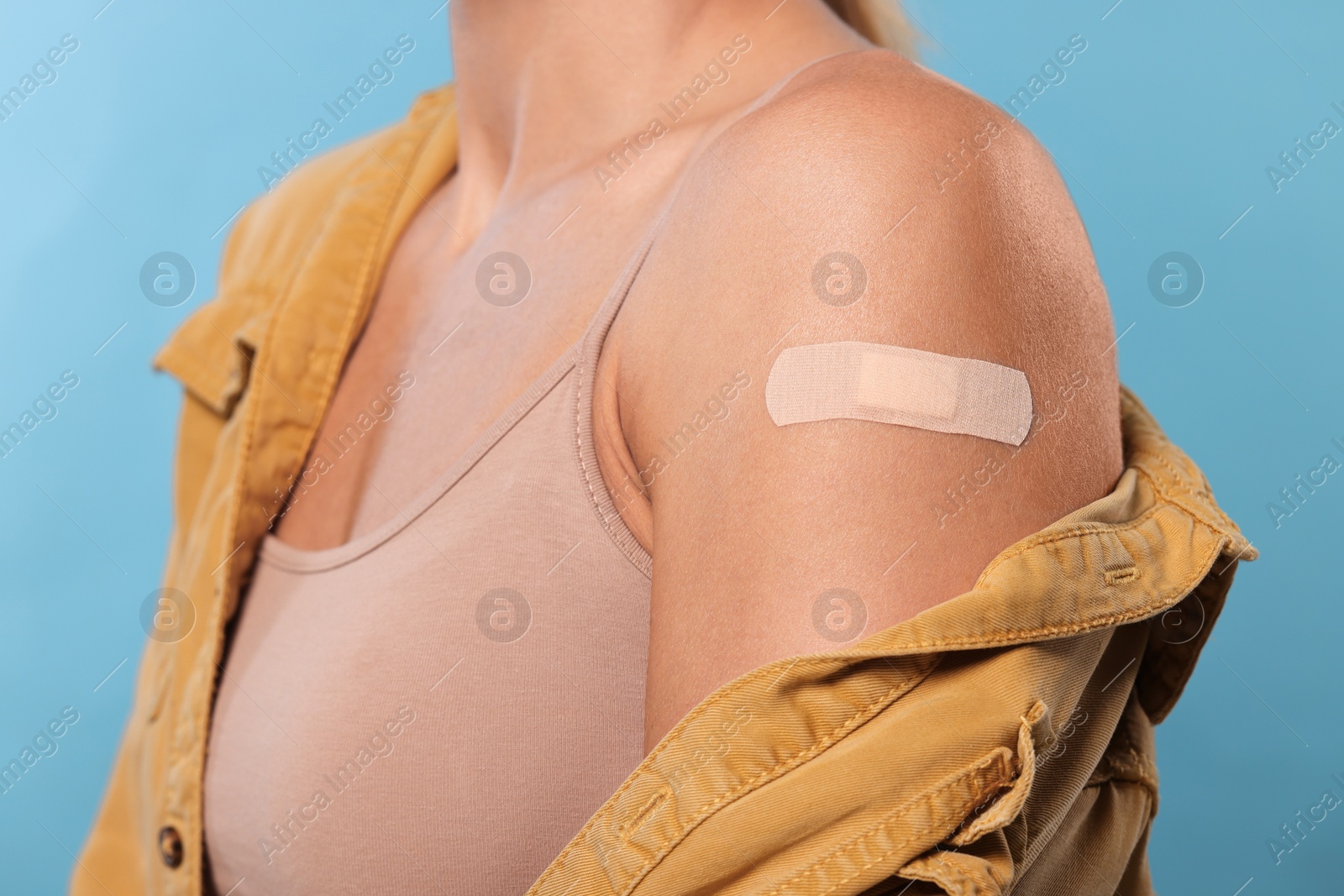 Photo of Woman with adhesive bandage on arm after vaccination on light blue background, closeup
