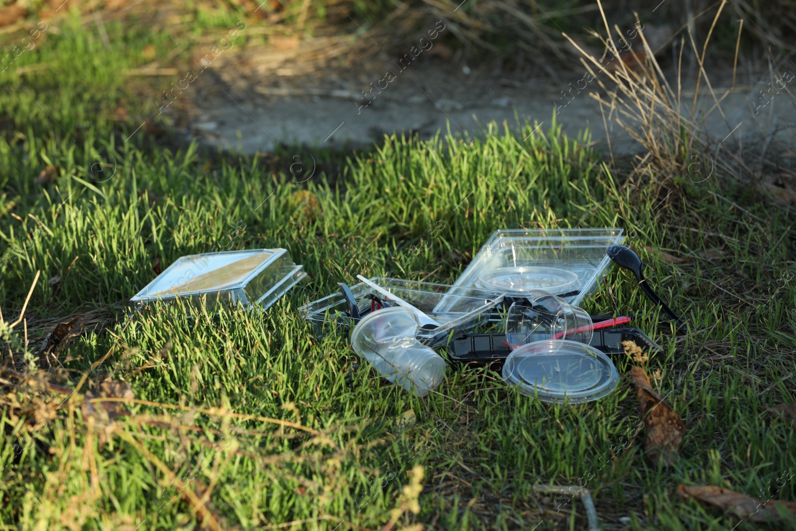 Photo of Used plastic tableware on grass outdoors. Environmental pollution concept