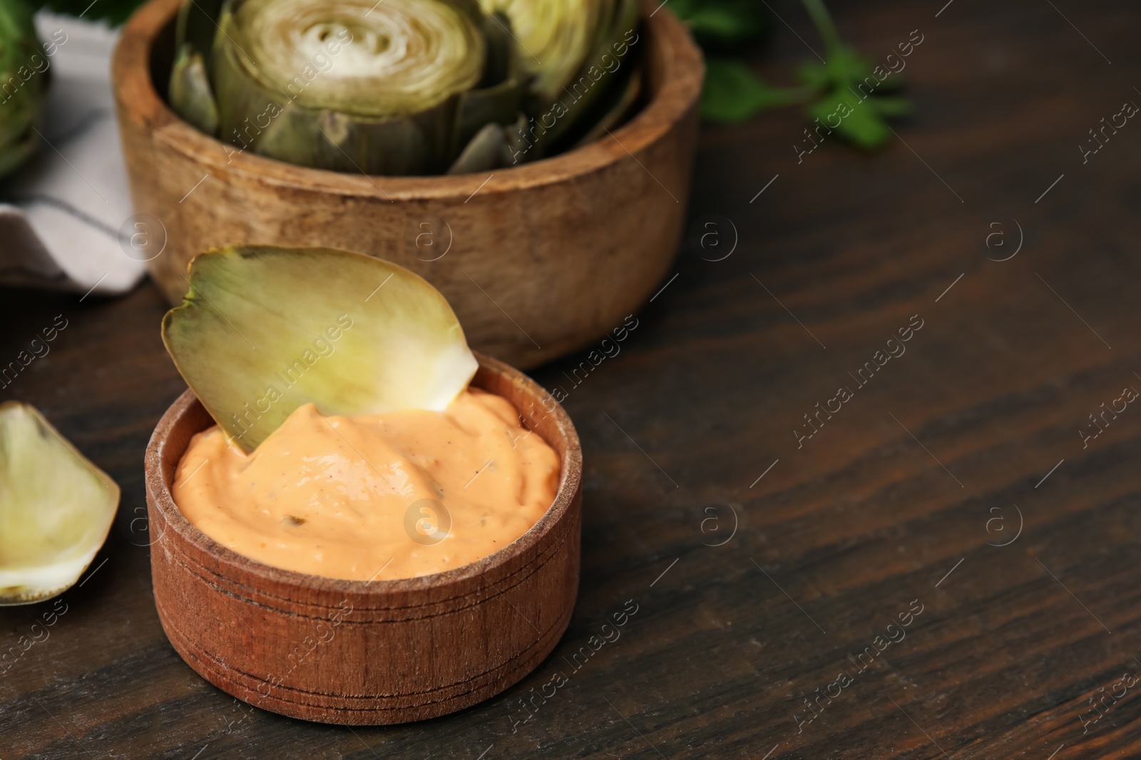 Photo of Delicious cooked artichoke with tasty sauce on wooden table, closeup. Space for text
