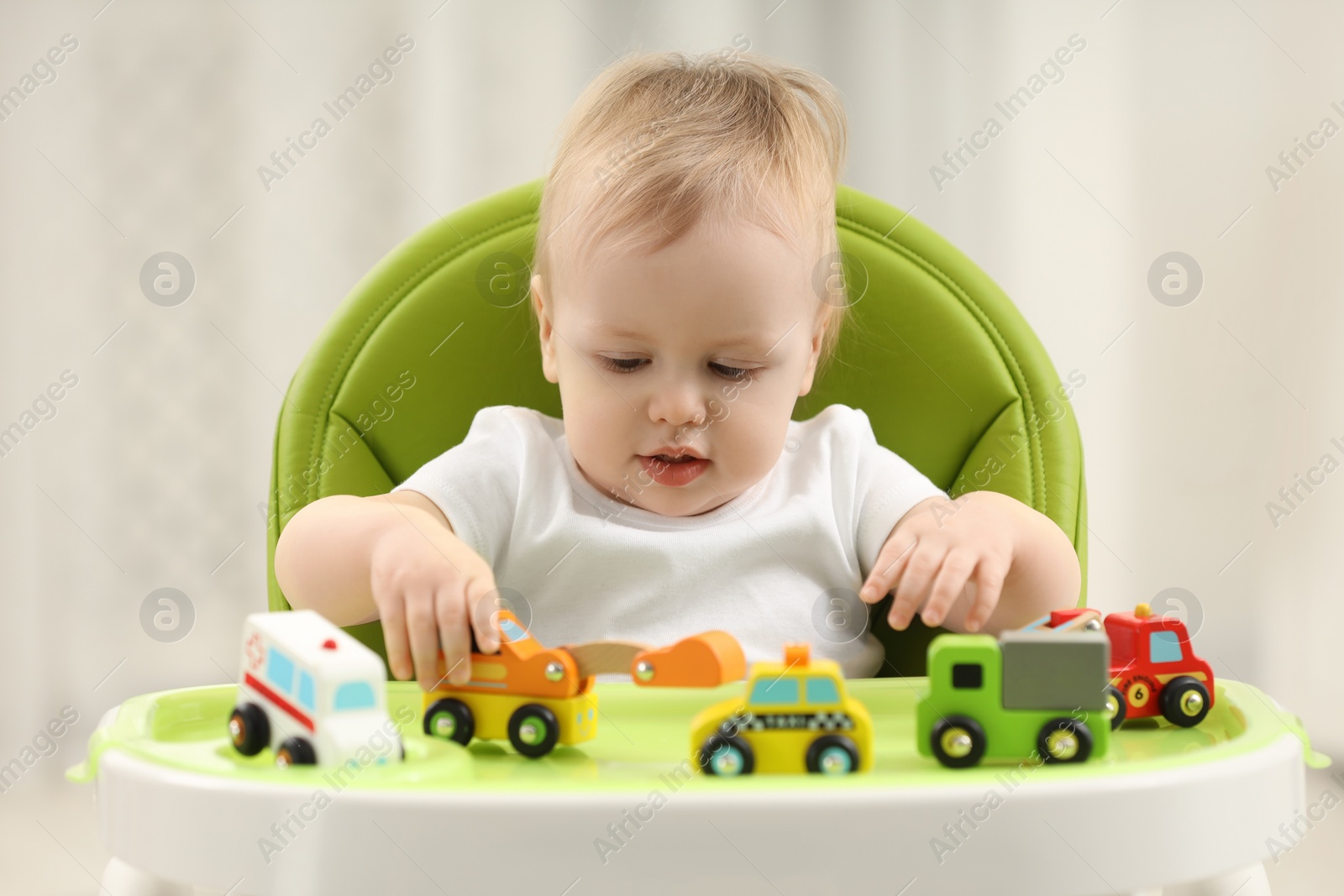 Photo of Children toys. Cute little boy playing with toy cars in high chair at home