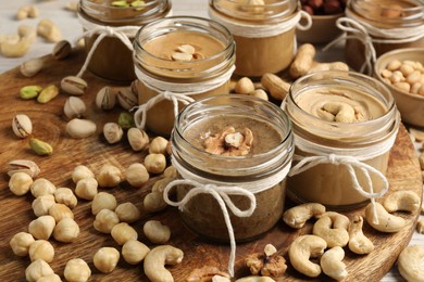 Tasty nut butters in jars and raw nuts on table, closeup