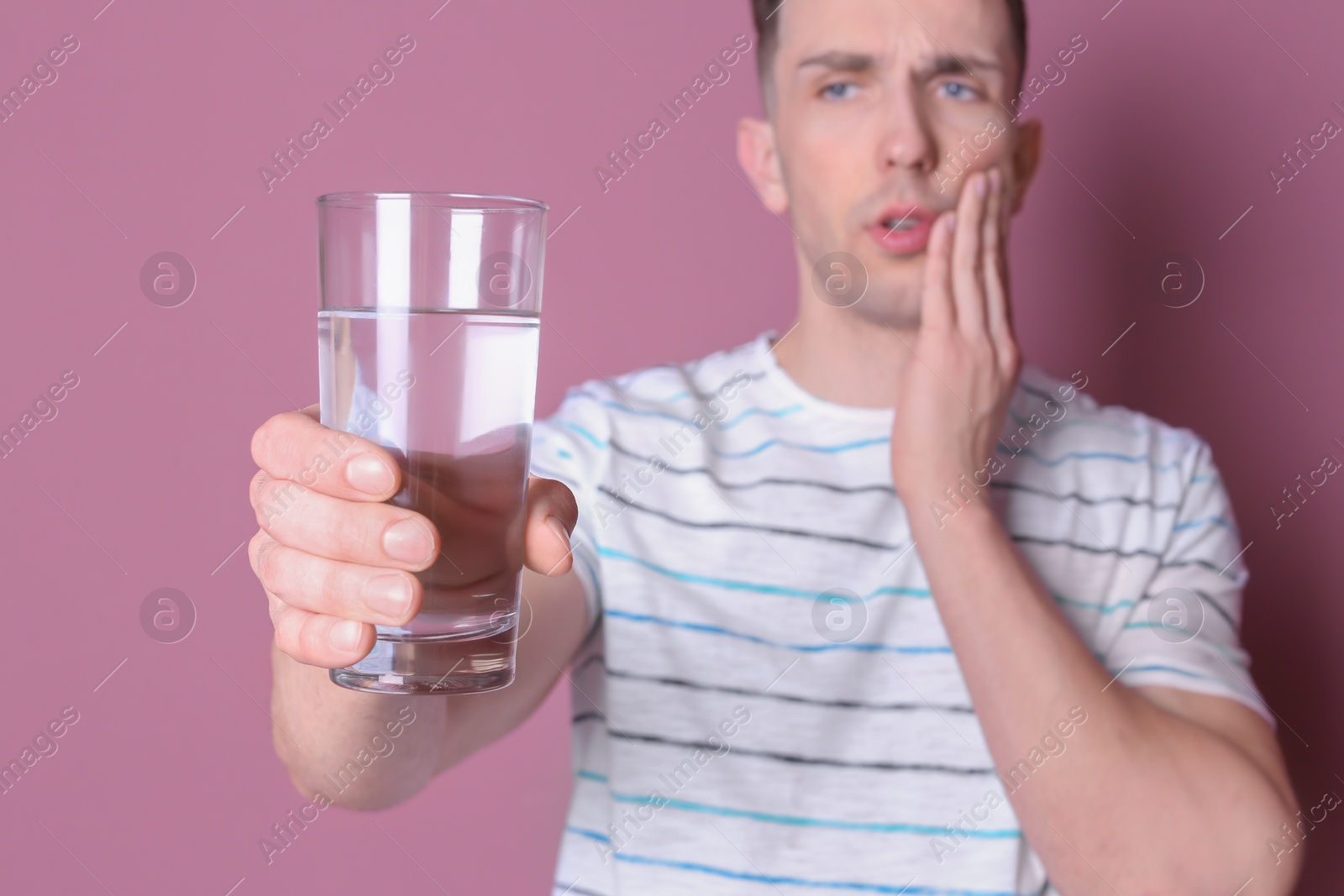 Photo of Young man with sensitive teeth and glass of cold water on color background