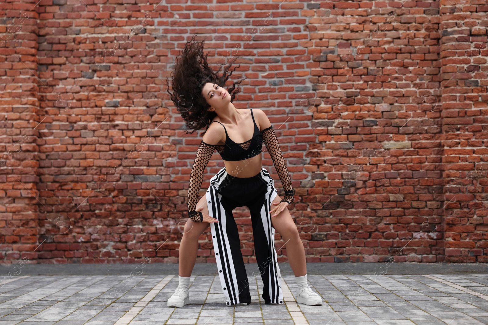 Photo of Beautiful young woman dancing hip hop near brick wall outdoors