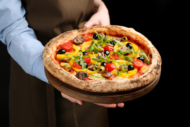 Woman holding tasty vegetable pizza on black background, closeup