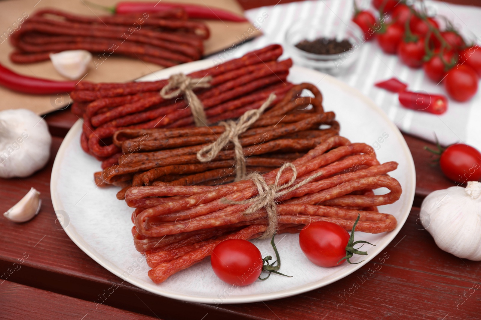 Photo of Bundles of delicious kabanosy with tomatoes on wooden table