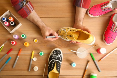 Photo of Man painting on sneaker at wooden table, top view. Customized shoes