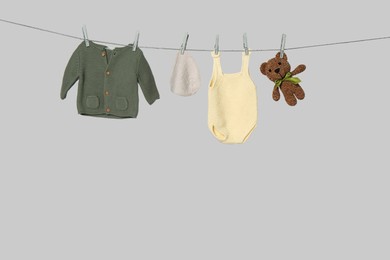 Photo of Different baby clothes and toy drying on laundry line against light background