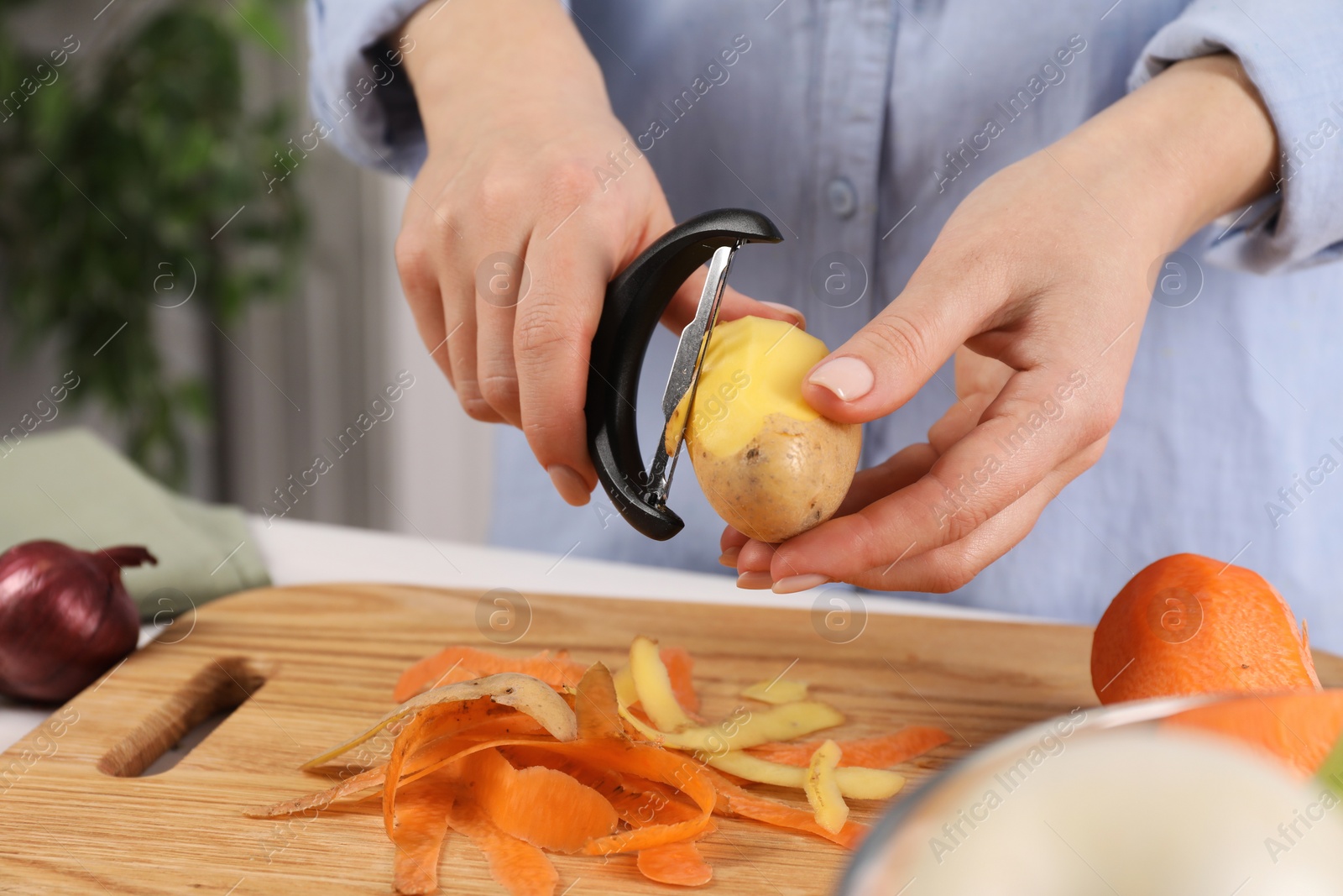 Photo of Woman peeling fresh potato at table indoors, closeup