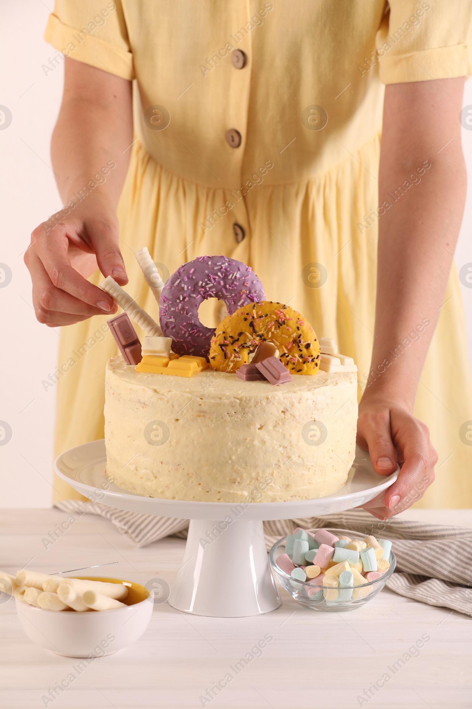 Photo of Woman decorating delicious cake with sweets at white wooden table, closeup