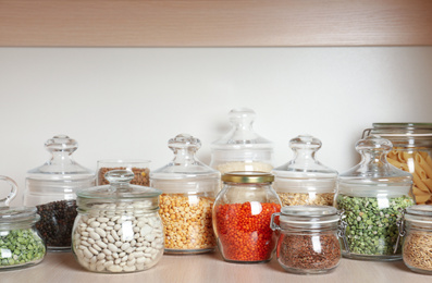 Glass jars with different types of groats on wooden shelf