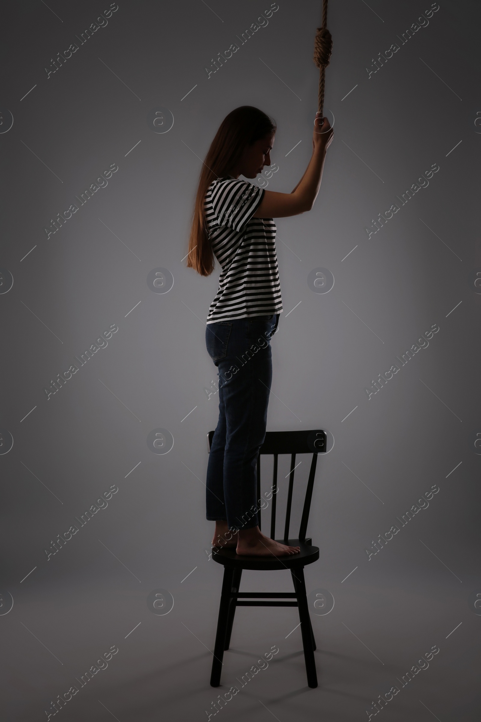 Photo of Depressed woman with rope noose standing on chair against grey background