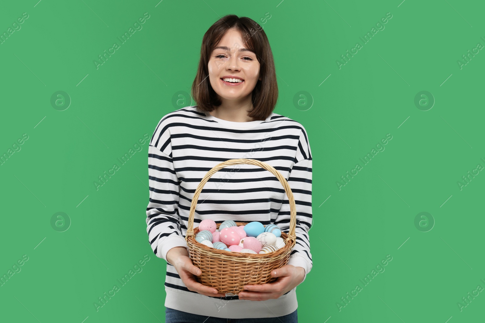 Photo of Easter celebration. Happy woman with wicker basket full of painted eggs on green background