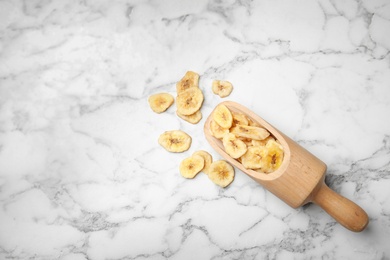 Photo of Scoop with banana slices on marble background, top view with space for text. Dried fruit as healthy snack