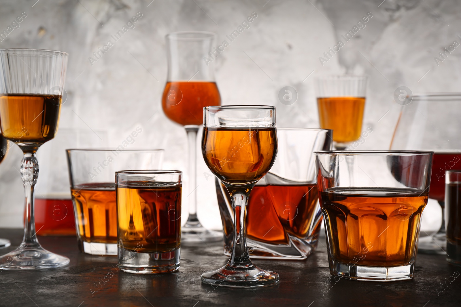 Photo of Different delicious liqueurs in glasses on grey table