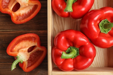 Ripe paprika peppers and crate on wooden background, top view