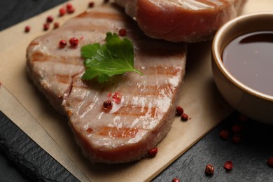 Photo of Delicious tuna steak with sauce, parsley and spices on board, closeup