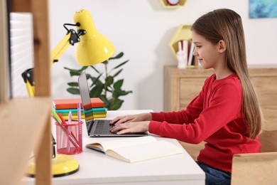 Photo of E-learning. Girl using laptop during online lesson at table indoors