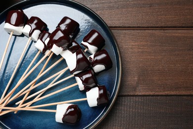 Photo of Delicious marshmallows covered with chocolate on wooden table, top view. Space for text