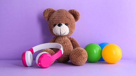 Baby songs. Toy bear, headphones and balls on violet background