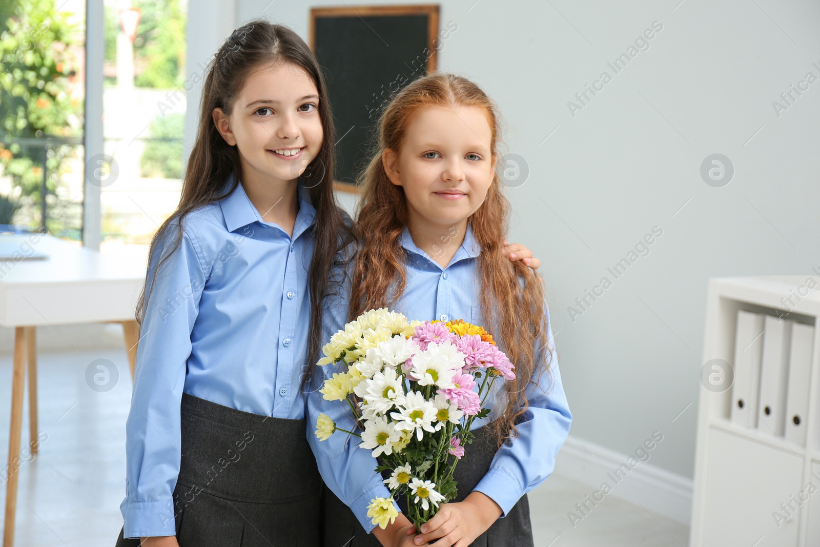 Photo of Happy schoolgirls with bouquet in classroom. Teacher's day