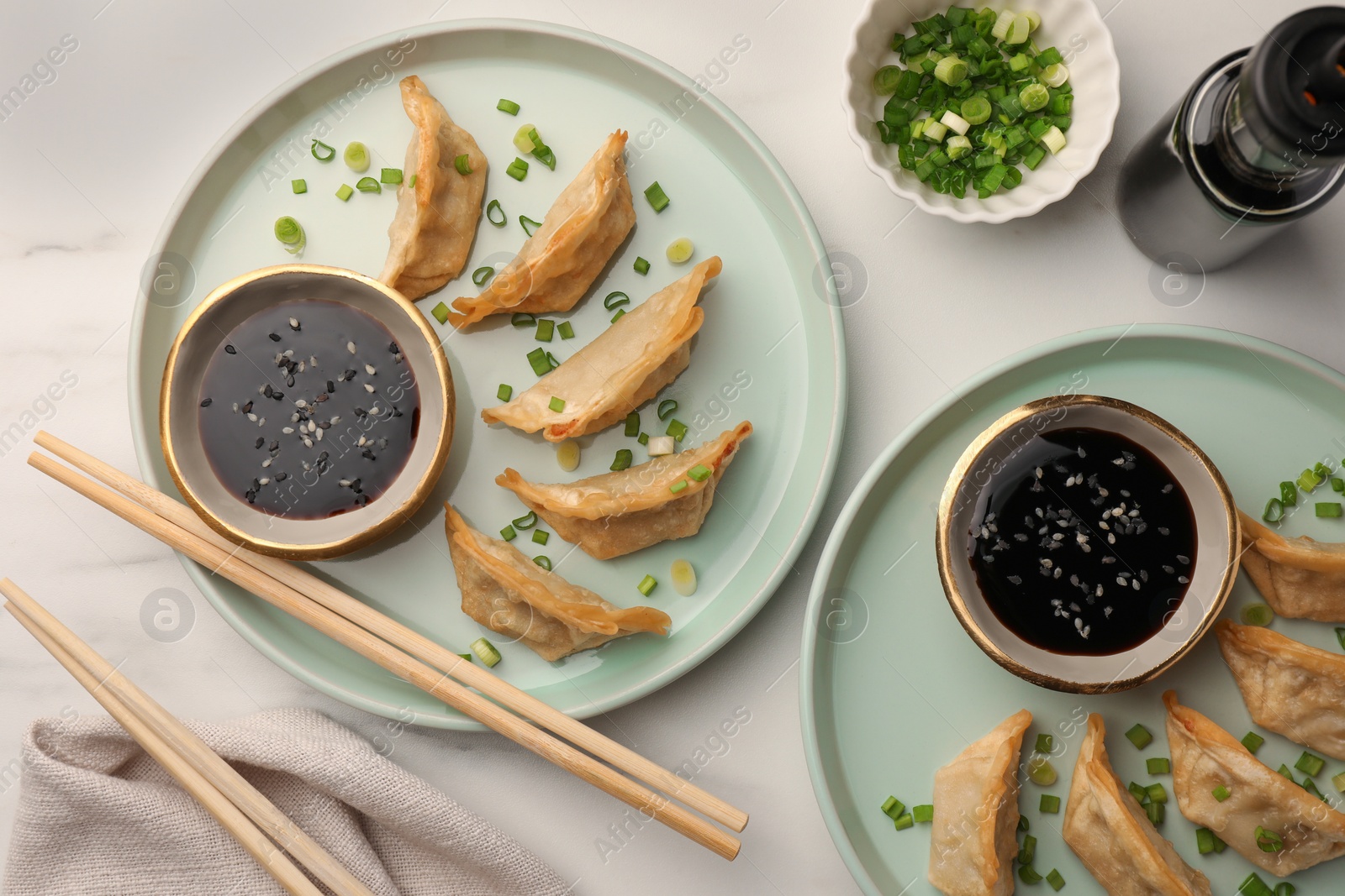 Photo of Delicious gyoza (asian dumplings) with soy sauce, green onions and chopsticks on white table, flat lay