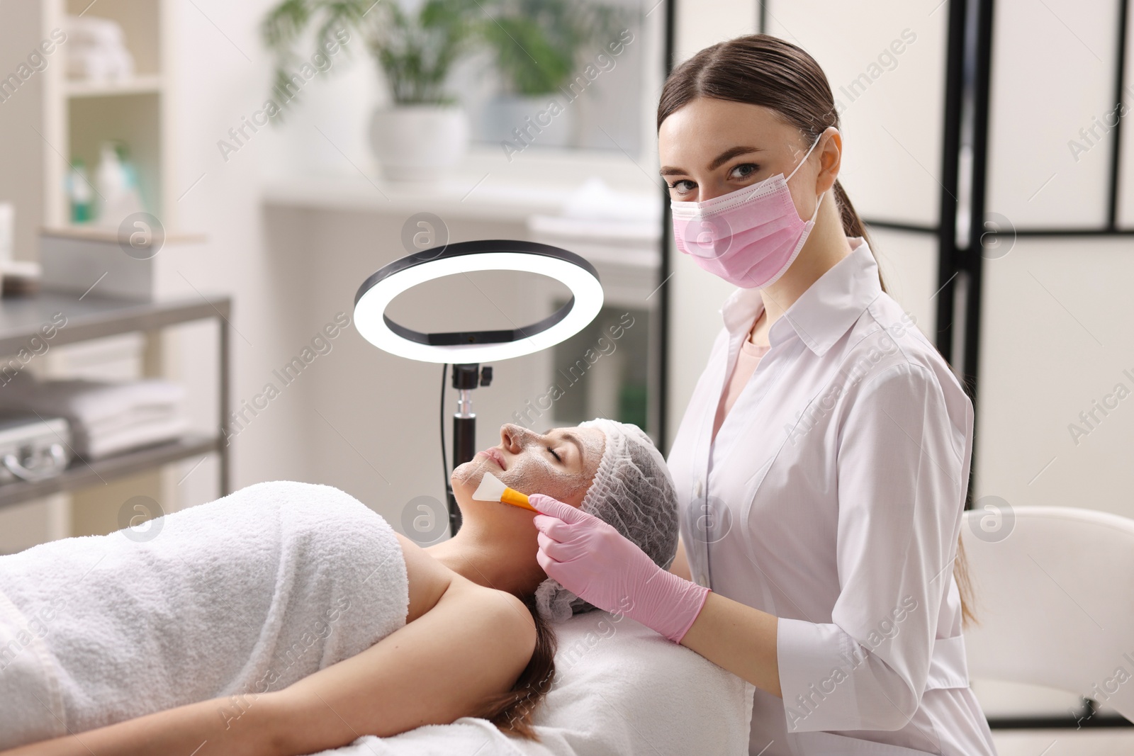 Photo of Cosmetologist applying mask on woman's face in clinic