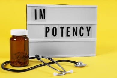 Photo of Lightbox with word IMPOTENCY, jar of pills and stethoscope on yellow background