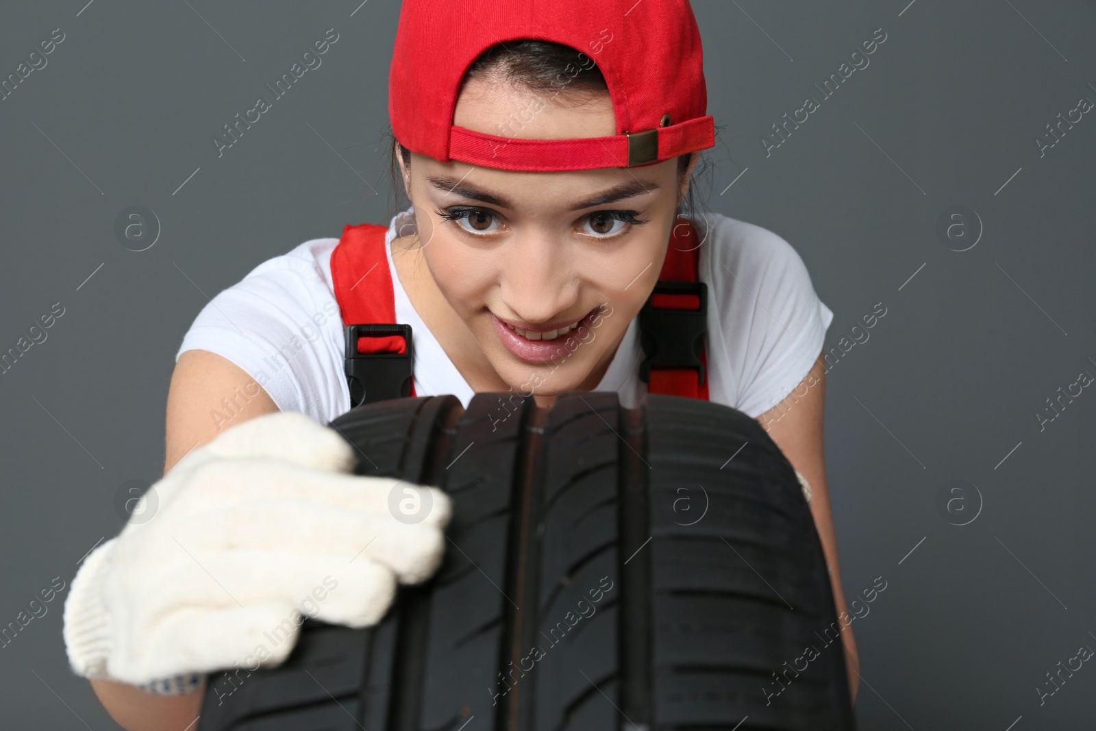 Photo of Female mechanic in uniform with car tire on grey background