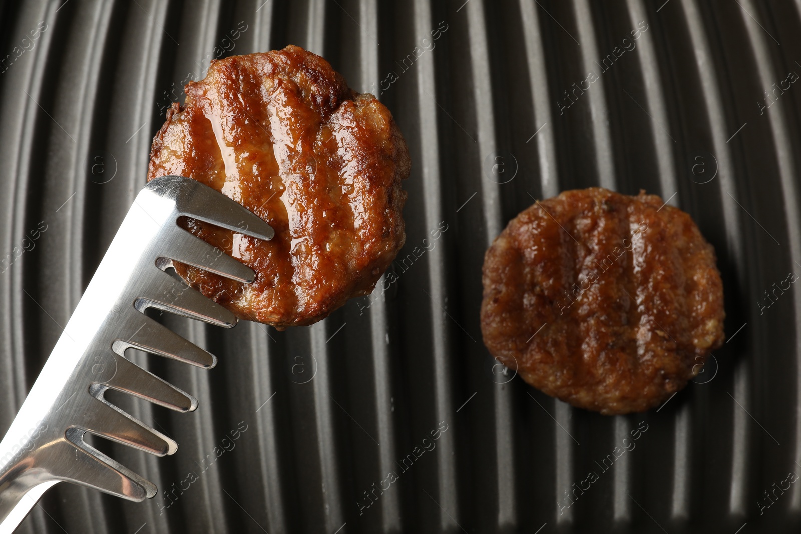 Photo of Taking delicious hamburger patty with tongs from electric grill, top view
