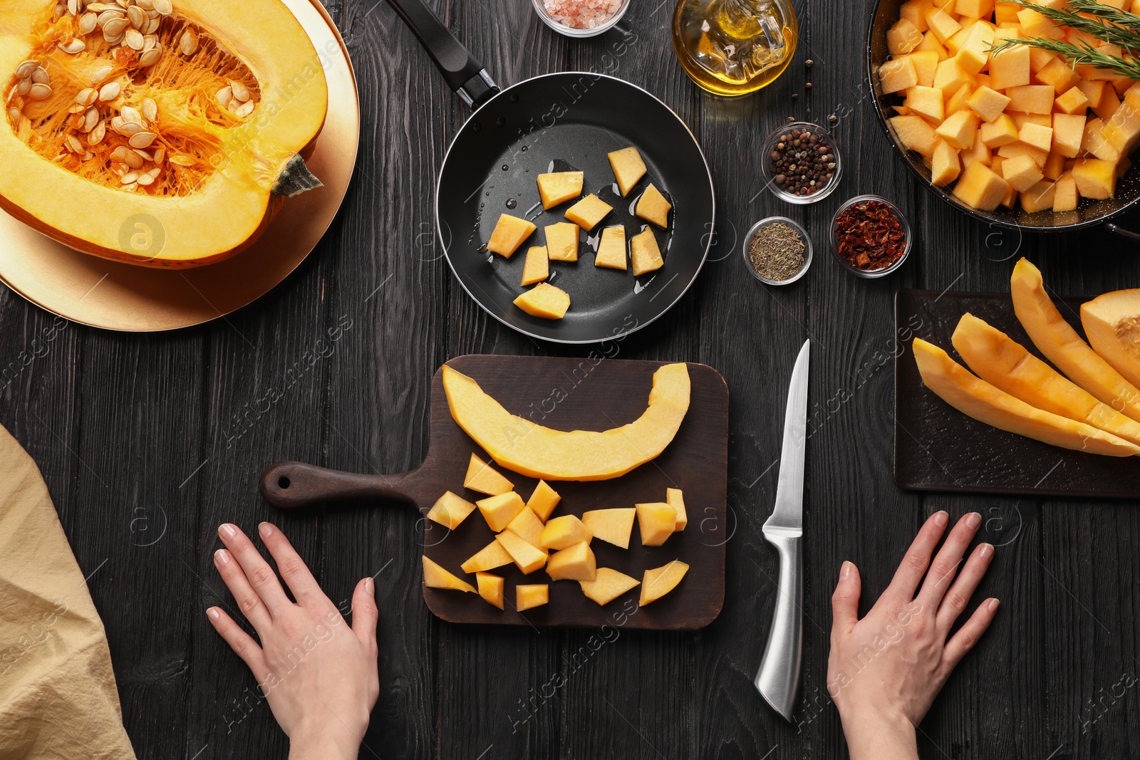 Photo of Woman and cut fresh pumpkin with different ingredients on black wooden table, top view