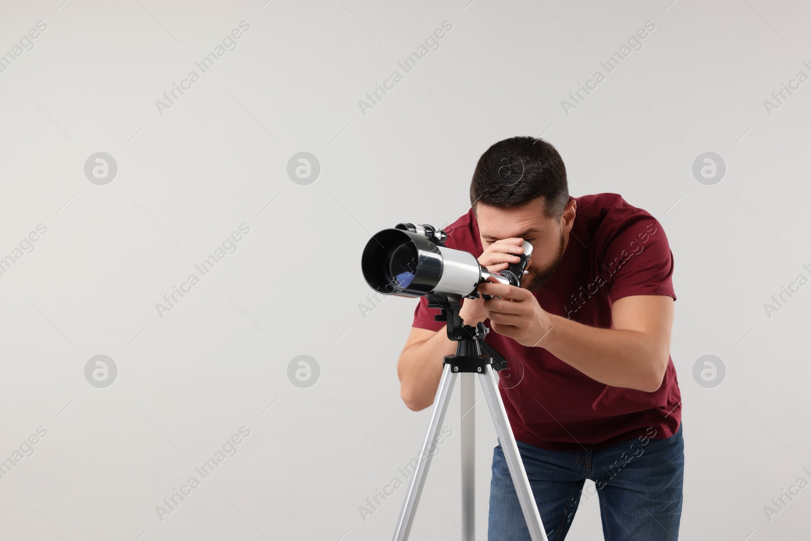 Photo of Astronomer looking at stars through telescope on light grey background. Space for text