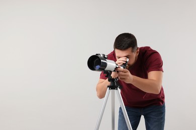 Photo of Astronomer looking at stars through telescope on light grey background. Space for text