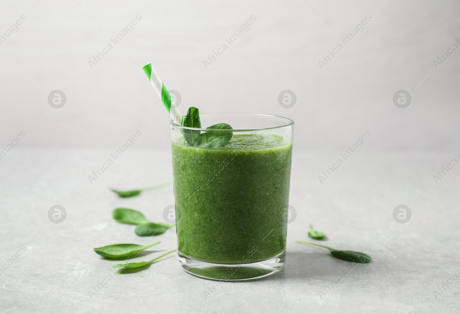 Photo of Green juice and fresh spinach leaves on light grey table