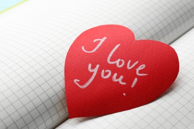 Photo of Paper heart with words I LOVE YOU on open notebook, closeup