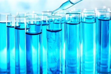 Dropping sample into test tube with blue liquid, closeup