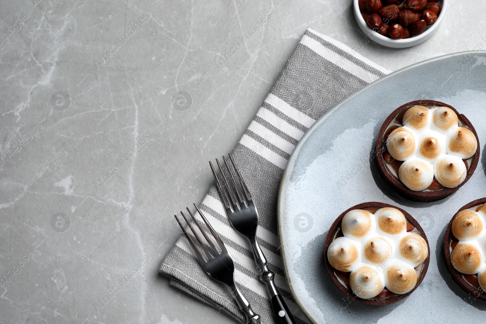Photo of Delicious salted caramel chocolate tarts with meringue and hazelnuts on light grey table, flat lay. Space for text