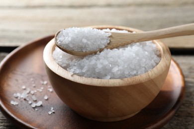 Photo of Organic salt in bowl and spoon on wooden table, closeup