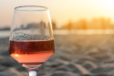 Photo of Glass of tasty rose wine on sand, closeup. Space for text