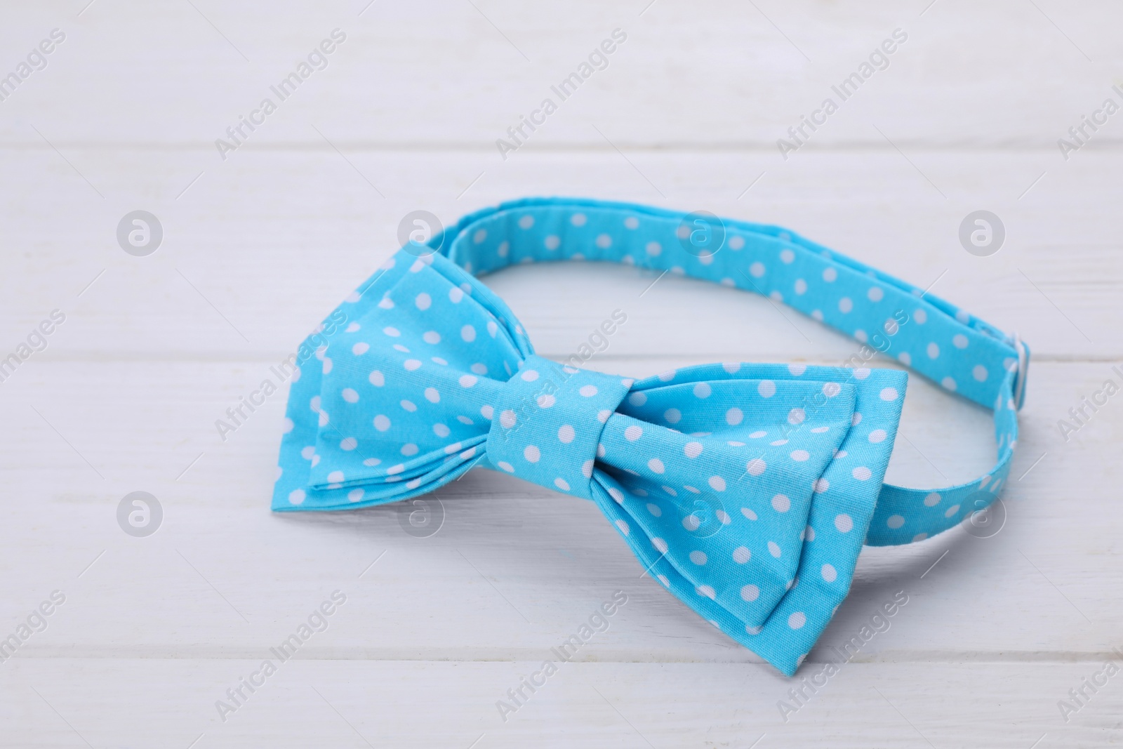 Photo of Stylish light blue bow tie with polka dot pattern on white wooden table, closeup