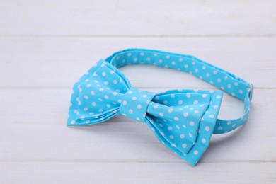Stylish light blue bow tie with polka dot pattern on white wooden table, closeup