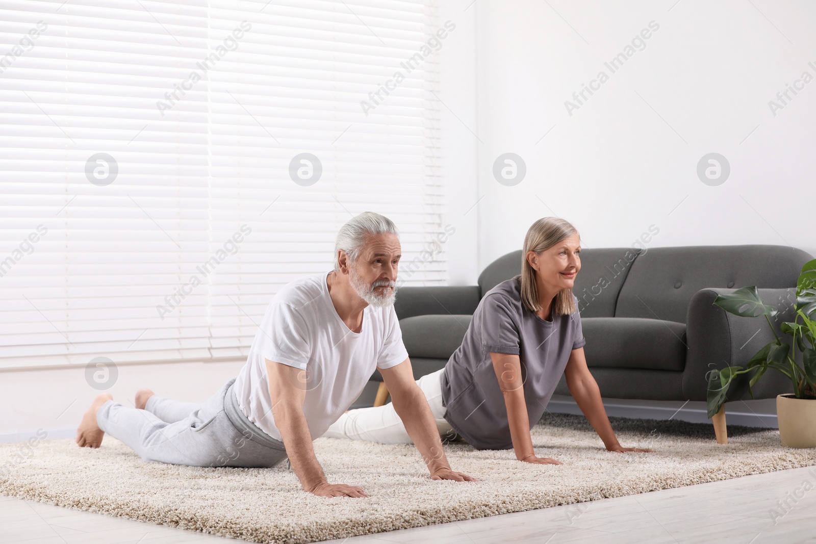 Photo of Senior couple practicing yoga on carpet at home. Healthy lifestyle