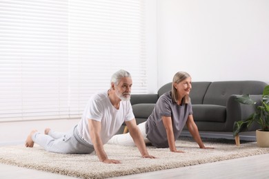 Senior couple practicing yoga on carpet at home. Healthy lifestyle