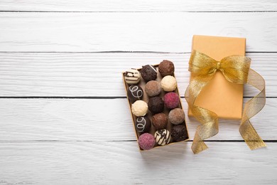 Photo of Open box with delicious chocolate candies on white wooden table, top view. Space for text