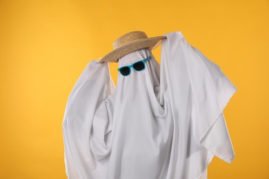 Photo of Person in ghost costume, sunglasses and straw hat on yellow background