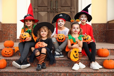 Photo of Cute little kids with pumpkins wearing Halloween costumes on stairs outdoors