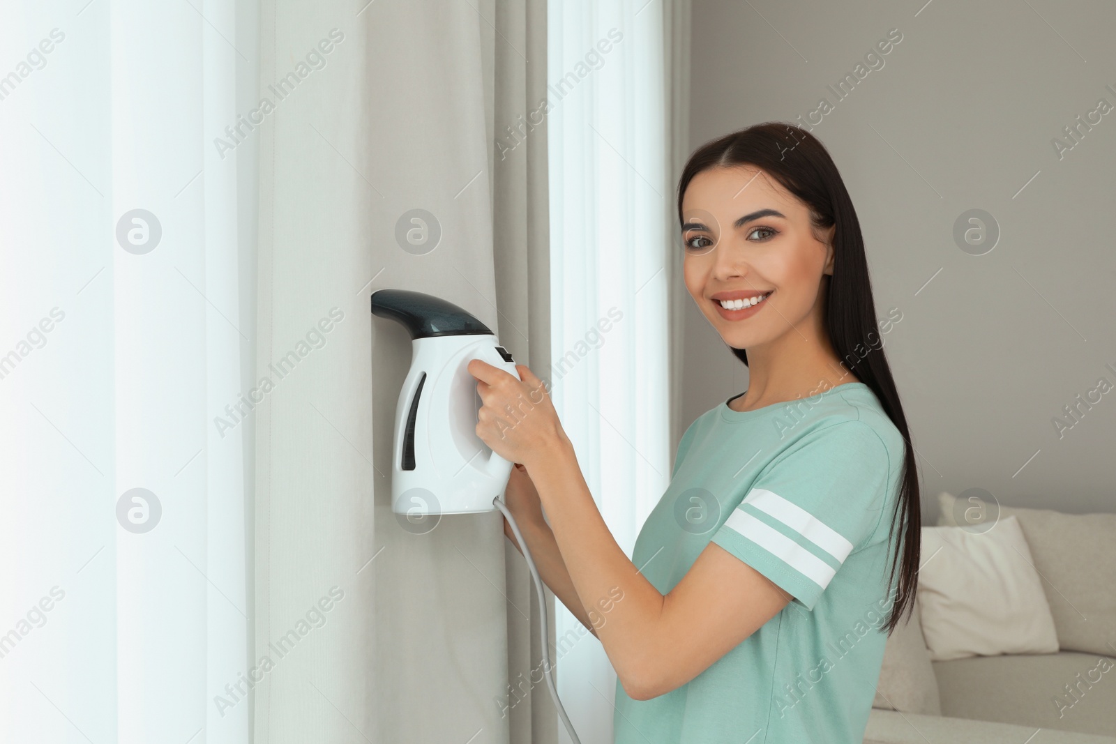 Photo of Woman steaming curtain near window at home. Space for text