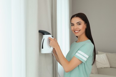 Woman steaming curtain near window at home. Space for text