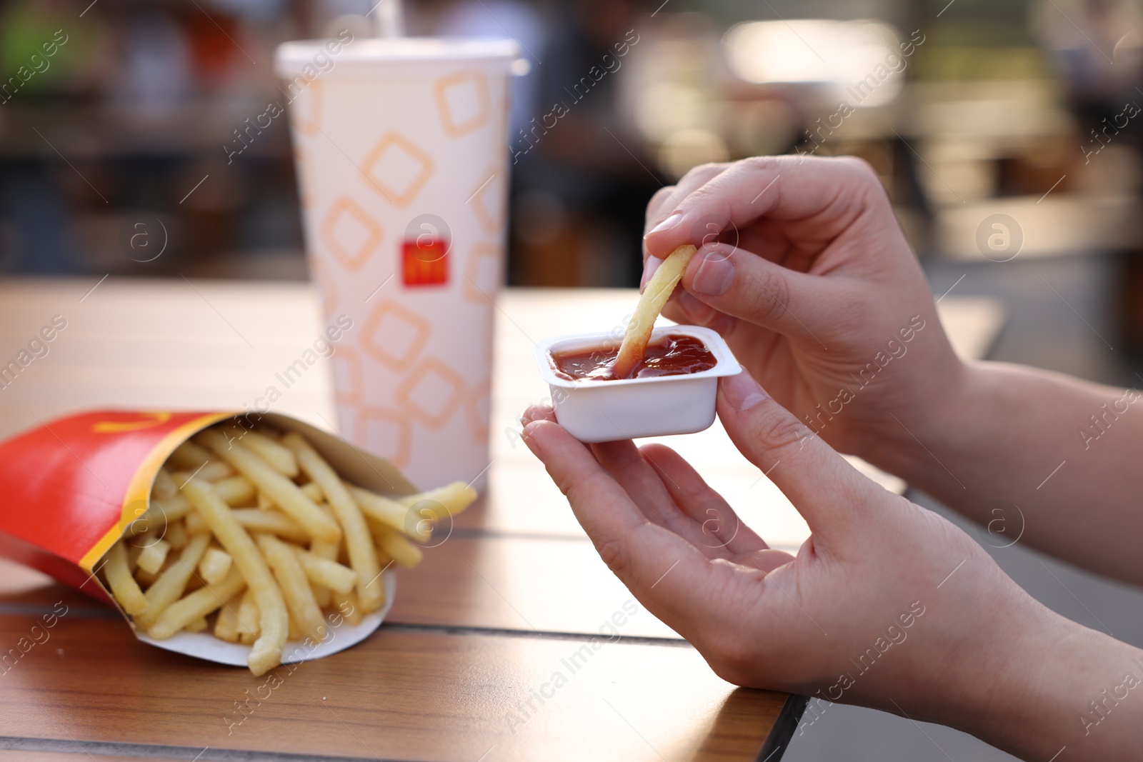 Photo of Lviv, Ukraine - September 26, 2023: Woman dipping McDonald's french fry into sauce at wooden table outdoors, closeup