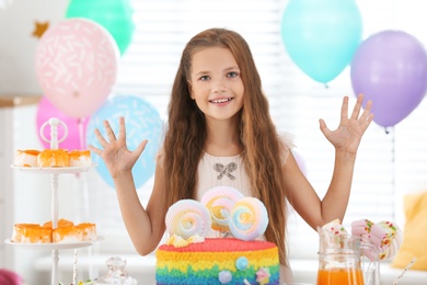 Photo of Happy girl at table with treats in room decorated for birthday party